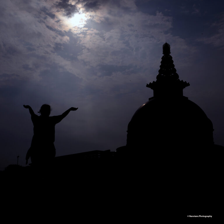 Silhouette of a figure with arms raised beside a stupa at dawn