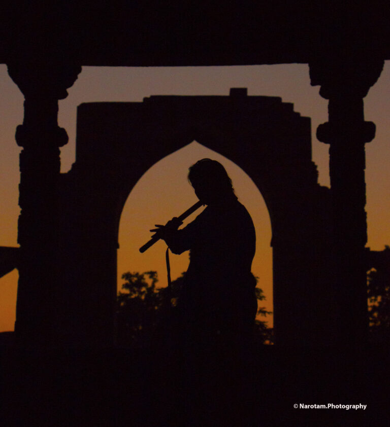 Silhouette of a flute player framed inside a stone arch at sunset