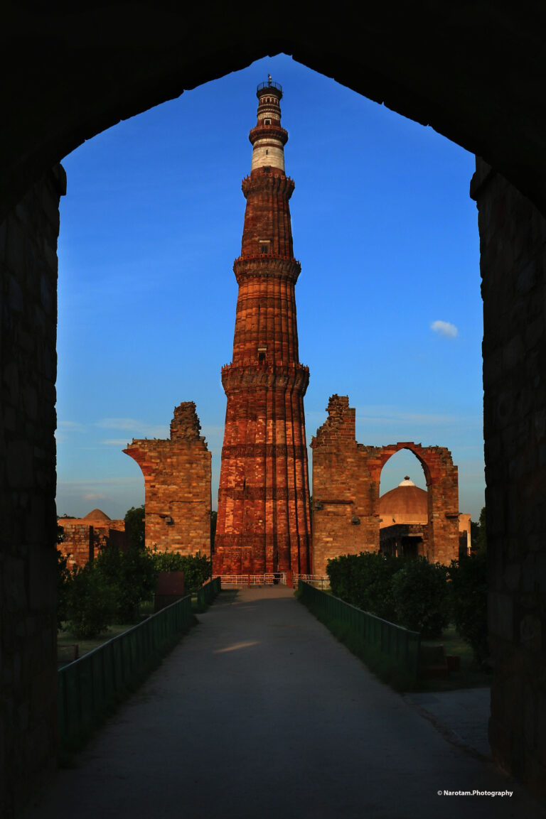 Qutub Minar framed by stone arches at dusk