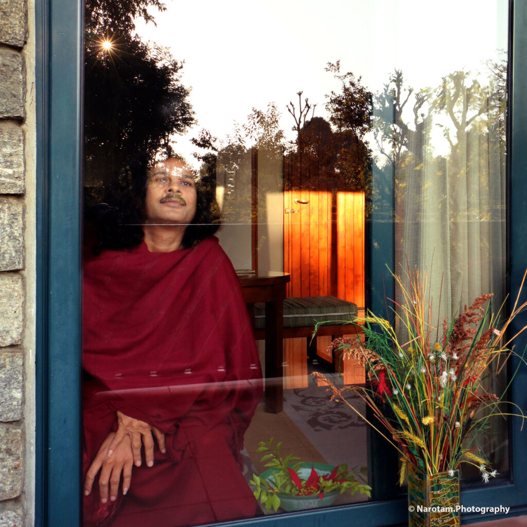 Monk in red robes seen through a window with reflected garden
